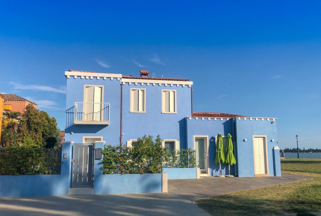 Bright blue residential building in Venice, Italy with clear skies and greenery.