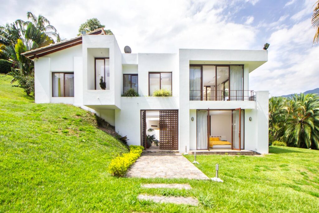 A contemporary white house surrounded by lush greenery on a hillside, showcasing modern architecture.